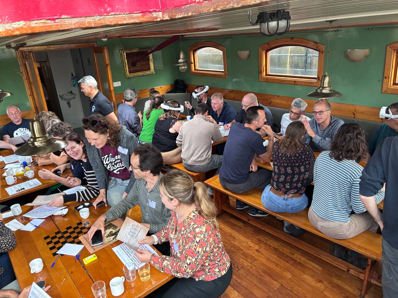 Medewerkers van het Ministerie van Landbouw overleggen en lachen tijdens de VR Escape Room op een schip in Harlingen